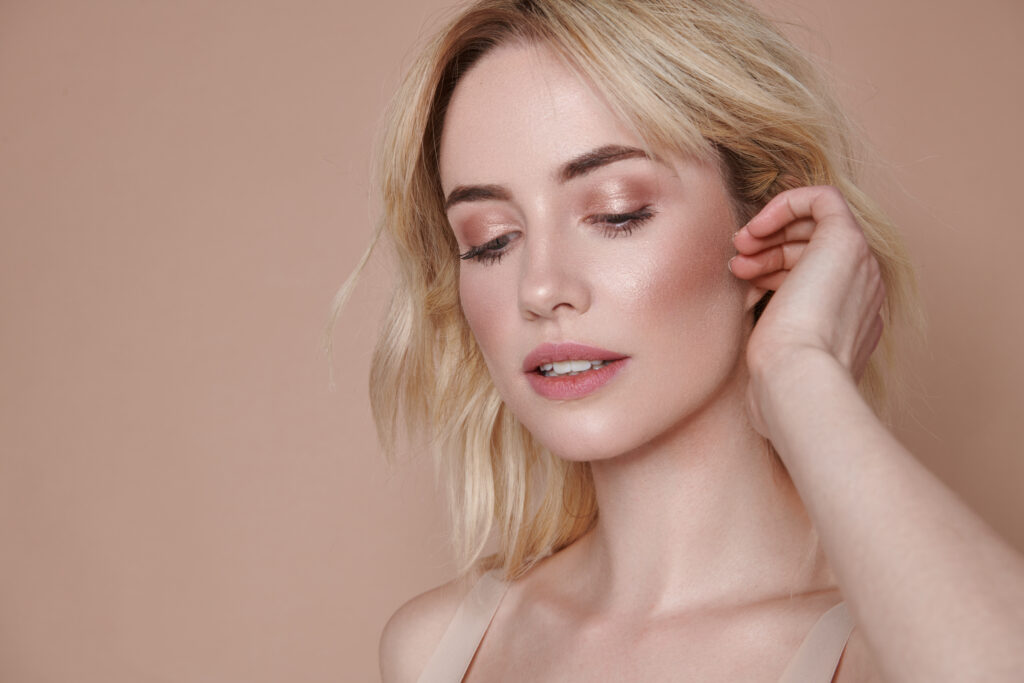 Woman with wavy blonde hair glancing down, against a warm blush background