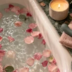Bath scattered with rose petals beside a lit candle, a folded towel and a sea-green vibrator