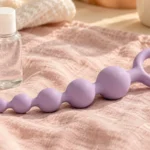 Lilac silicone anal beads with an external stop beside a lubricant bottle.