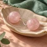 Two rose quartz kegel balls resting in a hand-shaped ceramic dish