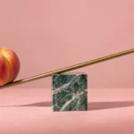 Peach on a brass rod balanced unevenly on a green marble block