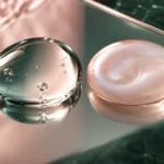 Two droplets on a mirror, one clear and one pearlescent pink